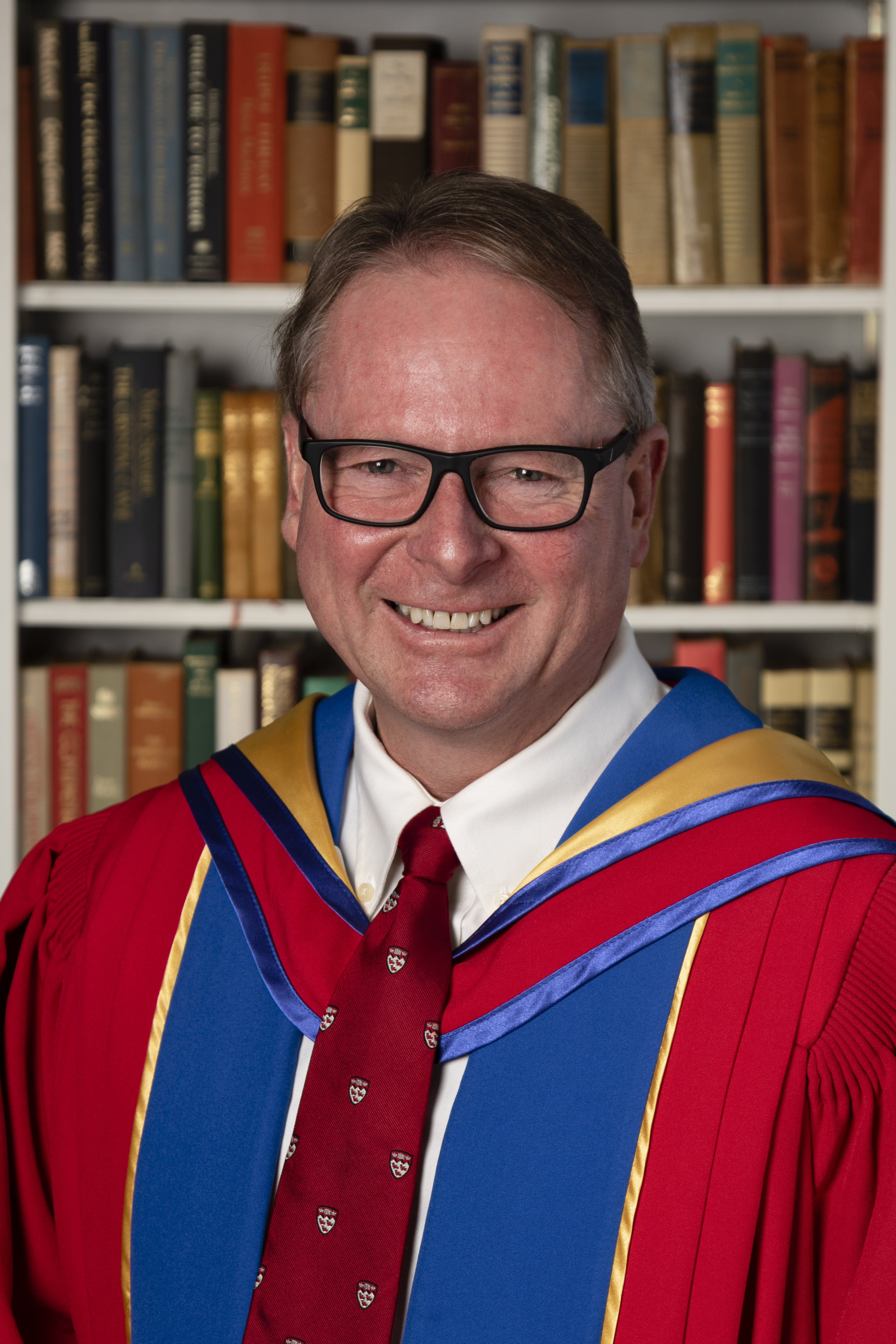 Man wearing glasses and a gown, in front of book shelf